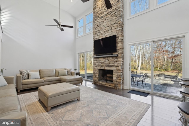 living room with a high ceiling, ceiling fan, a wealth of natural light, and a stone fireplace