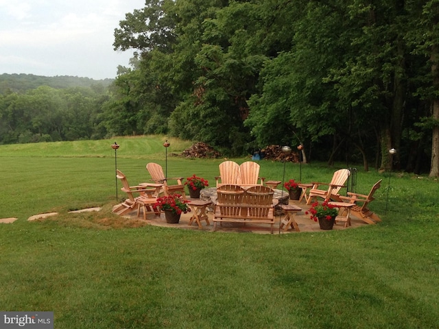 view of yard featuring a fire pit, a wooded view, and a patio area