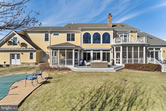 back of property with a balcony, a yard, a sunroom, and a chimney