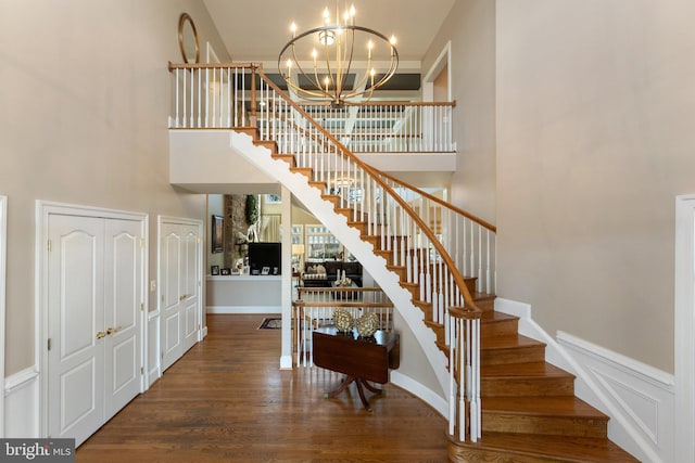 stairs with wood finished floors, a high ceiling, wainscoting, a decorative wall, and a chandelier