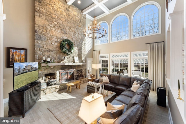 living room with coffered ceiling, a stone fireplace, a chandelier, and a healthy amount of sunlight