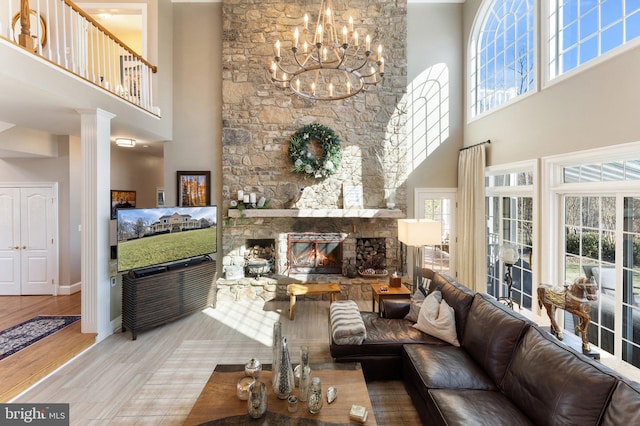 living area with baseboards, a chandelier, a stone fireplace, a high ceiling, and wood finished floors