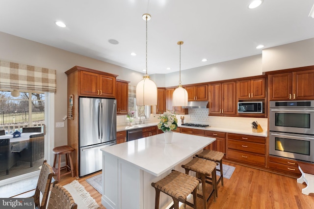 kitchen featuring a healthy amount of sunlight, under cabinet range hood, appliances with stainless steel finishes, light wood-type flooring, and backsplash