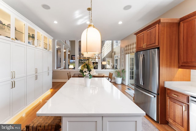 kitchen featuring light wood-type flooring, a kitchen island, stainless steel appliances, glass insert cabinets, and brown cabinets