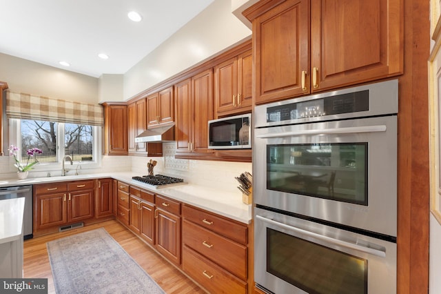 kitchen with tasteful backsplash, visible vents, under cabinet range hood, appliances with stainless steel finishes, and a sink