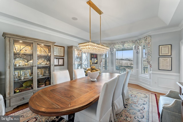 dining area featuring a tray ceiling, wood finished floors, wainscoting, a decorative wall, and a chandelier