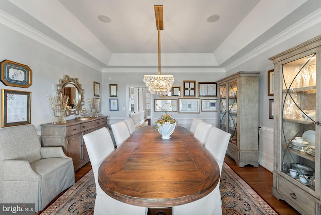 dining space with a tray ceiling, a notable chandelier, wood finished floors, and ornamental molding