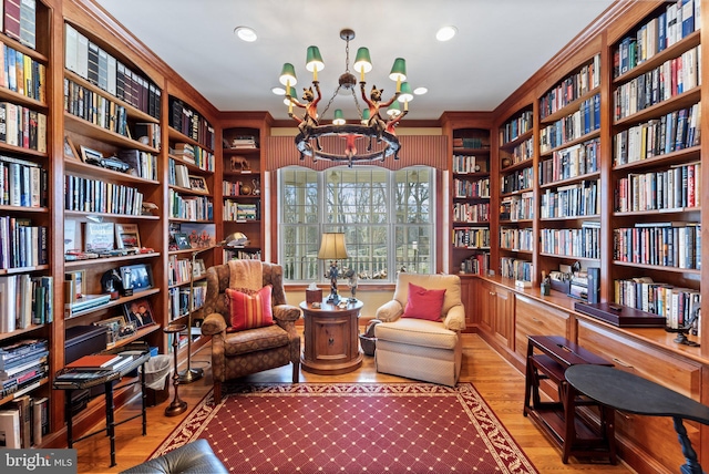 living area with a notable chandelier, ornamental molding, bookshelves, wood finished floors, and recessed lighting