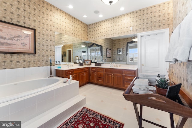 bathroom with wallpapered walls, a garden tub, double vanity, and a sink