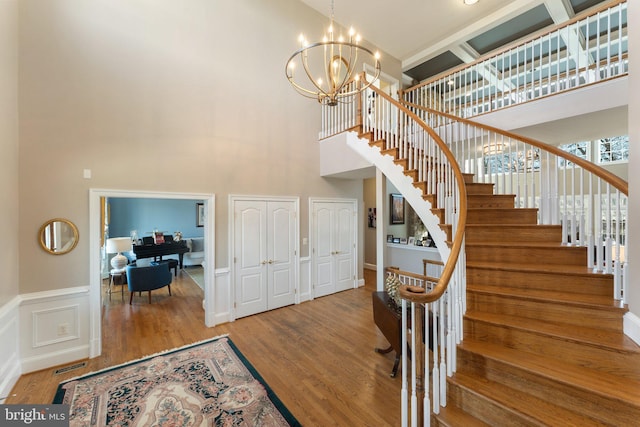 foyer entrance with a notable chandelier, stairway, visible vents, and wood finished floors