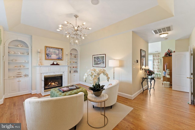 living area with visible vents, built in shelves, a high end fireplace, light wood-style floors, and baseboards