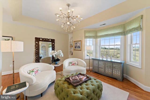 living area featuring visible vents, a tray ceiling, wood finished floors, an inviting chandelier, and baseboards