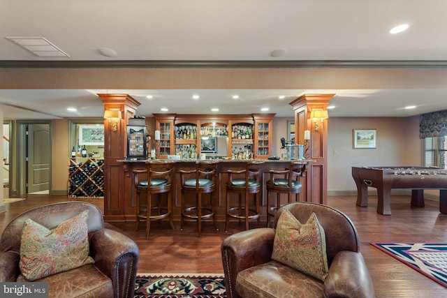 bar with bar area, wood finished floors, ornate columns, and ornamental molding