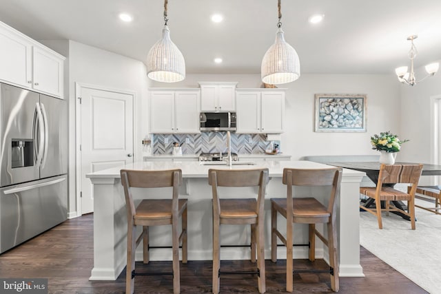 kitchen featuring appliances with stainless steel finishes, pendant lighting, an island with sink, and white cabinets