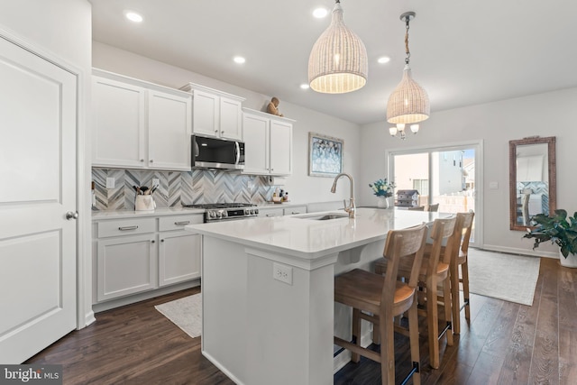 kitchen with stainless steel appliances, sink, white cabinetry, hanging light fixtures, and a center island with sink