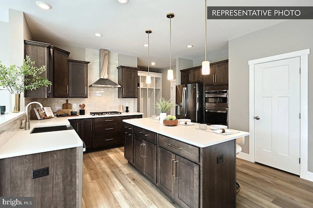 kitchen with dark brown cabinetry, appliances with stainless steel finishes, wall chimney range hood, and a sink