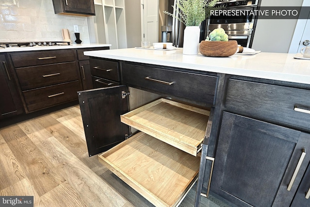 kitchen featuring stainless steel appliances, decorative backsplash, light countertops, dark brown cabinetry, and light wood-style floors