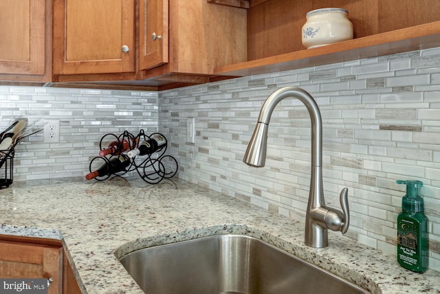 room details featuring sink, light stone counters, and backsplash