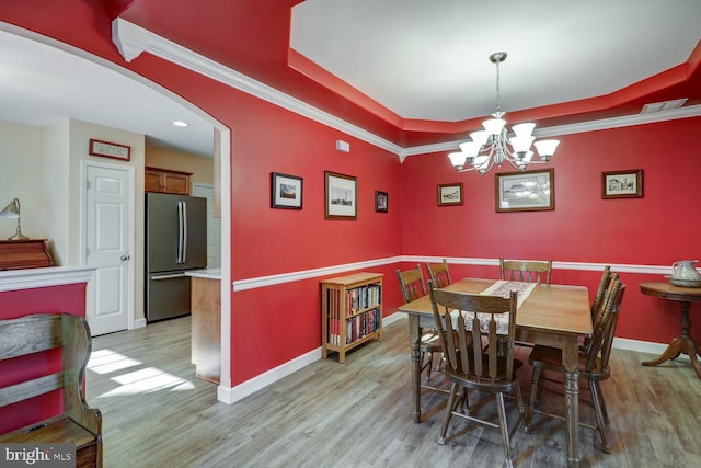 dining room with a raised ceiling, an inviting chandelier, crown molding, and light hardwood / wood-style flooring