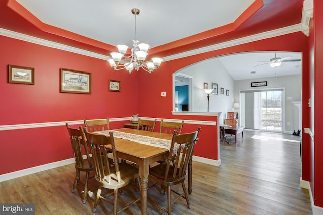 dining room with ceiling fan with notable chandelier, hardwood / wood-style flooring, a raised ceiling, and lofted ceiling