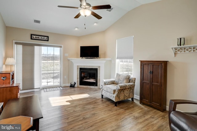 living area featuring a tiled fireplace, ceiling fan, light hardwood / wood-style flooring, and a healthy amount of sunlight