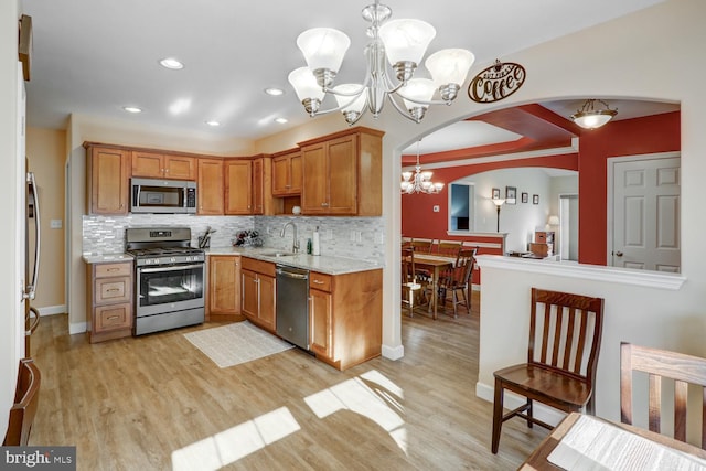 kitchen featuring sink, decorative light fixtures, light hardwood / wood-style floors, decorative backsplash, and appliances with stainless steel finishes