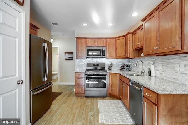 kitchen featuring appliances with stainless steel finishes, light hardwood / wood-style floors, light stone countertops, decorative backsplash, and sink