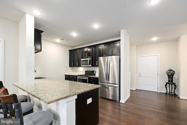 kitchen featuring light stone countertops, dark hardwood / wood-style flooring, stainless steel appliances, decorative backsplash, and a breakfast bar