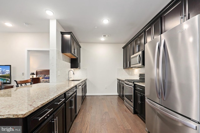 kitchen with appliances with stainless steel finishes, backsplash, wood-type flooring, light stone countertops, and sink