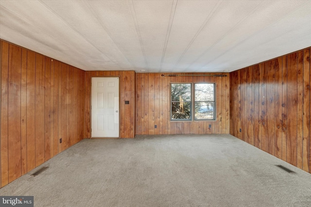 empty room with carpet floors, wooden walls, and a textured ceiling