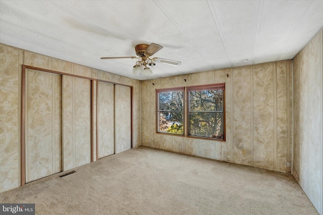 unfurnished bedroom featuring ceiling fan, multiple closets, and light carpet