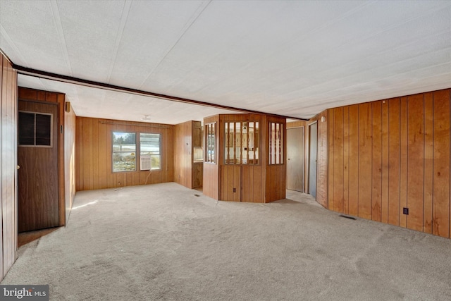 empty room with a textured ceiling, light carpet, and wood walls