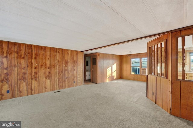 spare room featuring light carpet, wood walls, and a textured ceiling