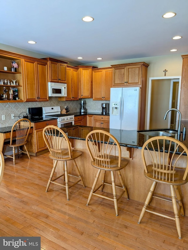 kitchen featuring white appliances, light hardwood / wood-style floors, decorative backsplash, a breakfast bar area, and sink