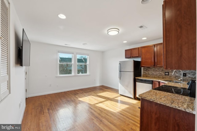 kitchen with sink, light hardwood / wood-style flooring, appliances with stainless steel finishes, light stone countertops, and decorative backsplash