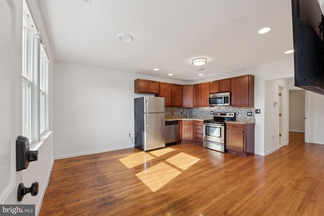 kitchen with tasteful backsplash, stainless steel appliances, and light hardwood / wood-style flooring