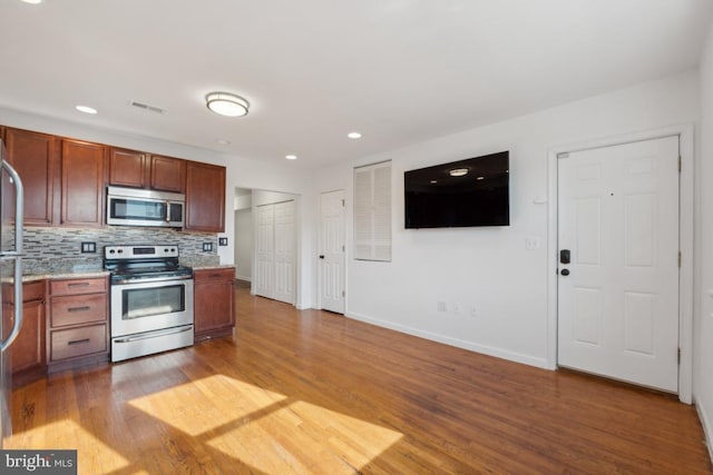 kitchen featuring hardwood / wood-style flooring, light stone countertops, appliances with stainless steel finishes, and backsplash