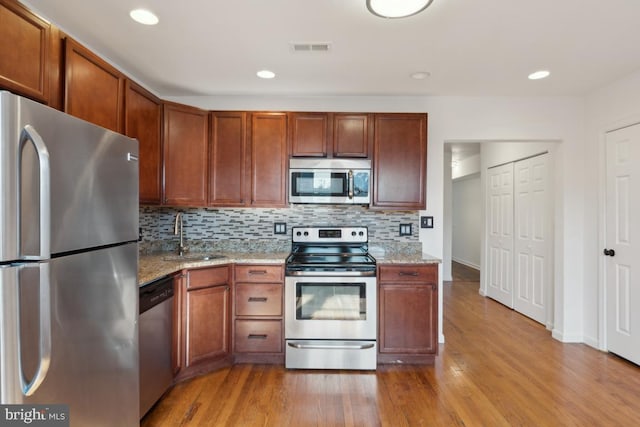 kitchen featuring appliances with stainless steel finishes, sink, light stone counters, and light hardwood / wood-style floors