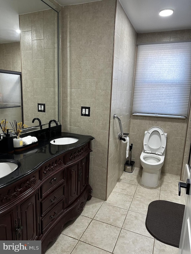 bathroom with toilet, vanity, tile patterned floors, and tile walls