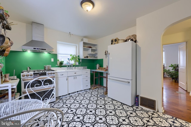 kitchen featuring white refrigerator, sink, white cabinets, stainless steel gas range, and wall chimney exhaust hood