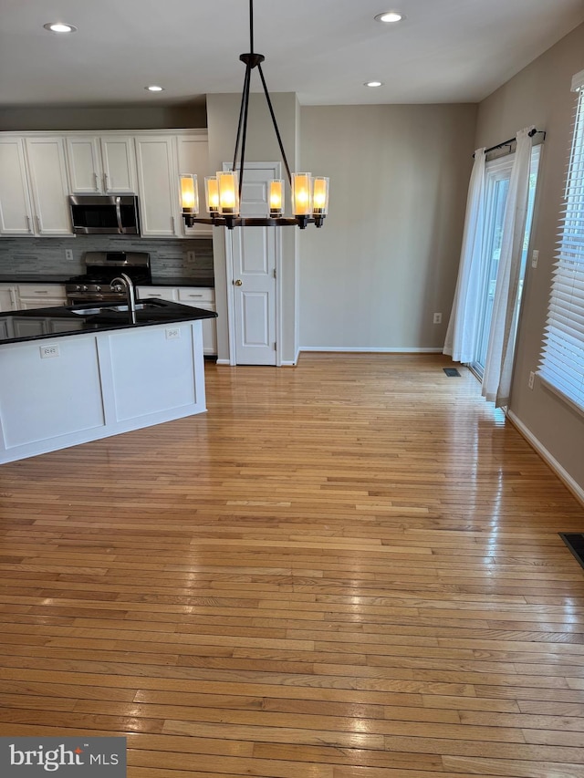 kitchen featuring dark countertops, tasteful backsplash, white cabinetry, stainless steel appliances, and light wood finished floors