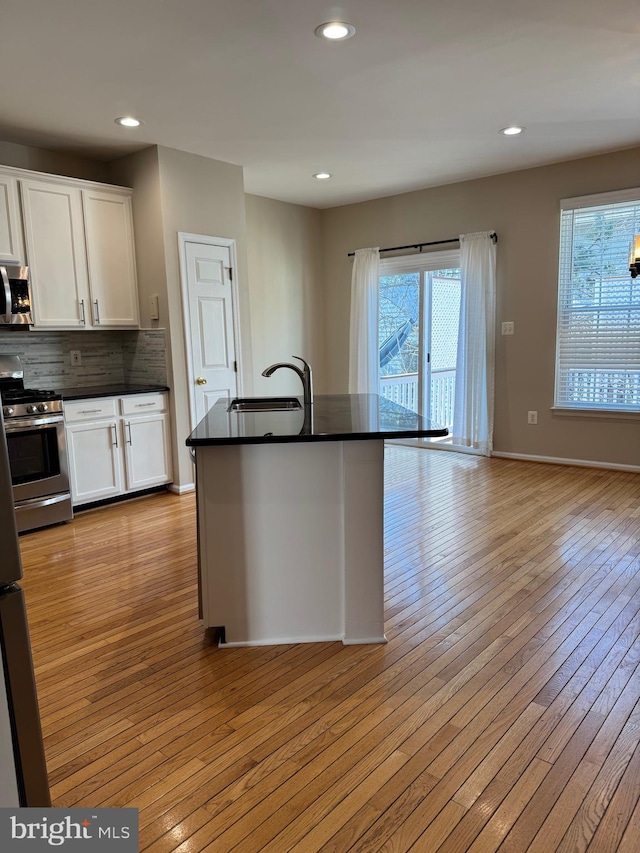 kitchen with dark countertops, light wood-type flooring, stainless steel appliances, white cabinetry, and a sink