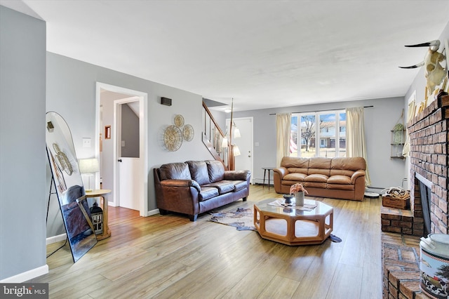 living room with a brick fireplace, a baseboard heating unit, and light hardwood / wood-style flooring