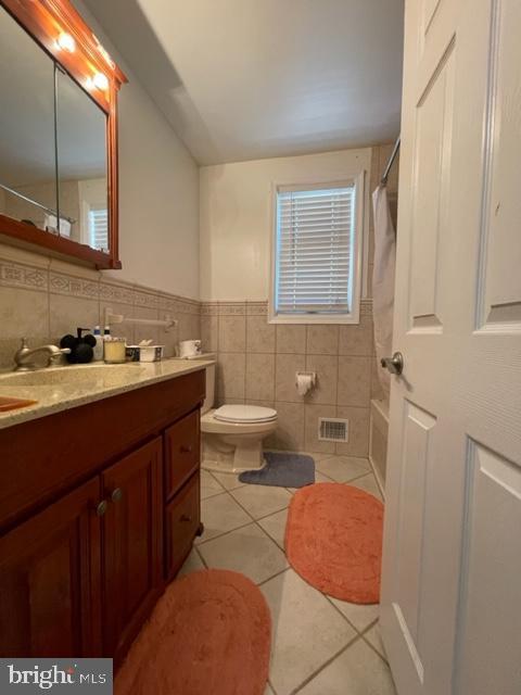 bathroom featuring curtained shower, tile patterned flooring, toilet, vanity, and tile walls