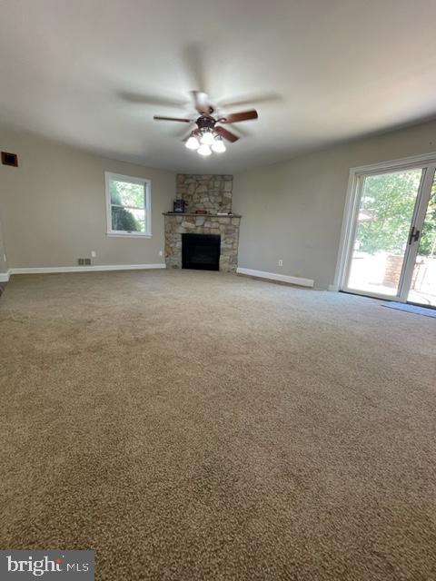 unfurnished living room featuring carpet flooring, a stone fireplace, and ceiling fan