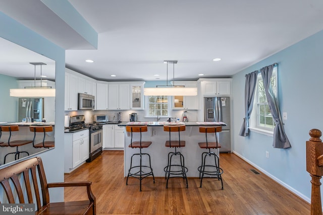 kitchen featuring pendant lighting, white cabinets, appliances with stainless steel finishes, hardwood / wood-style floors, and a kitchen breakfast bar