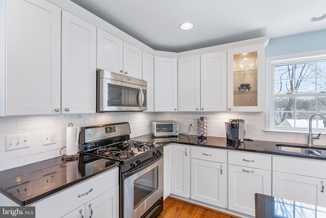 kitchen with appliances with stainless steel finishes, sink, backsplash, white cabinetry, and plenty of natural light