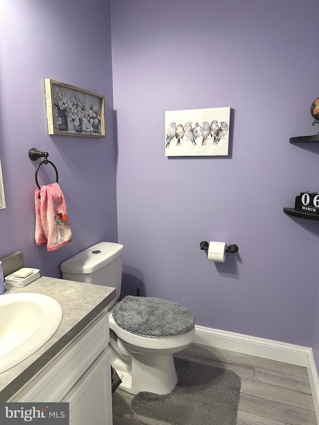 half bath with wood finished floors, vanity, toilet, and baseboards