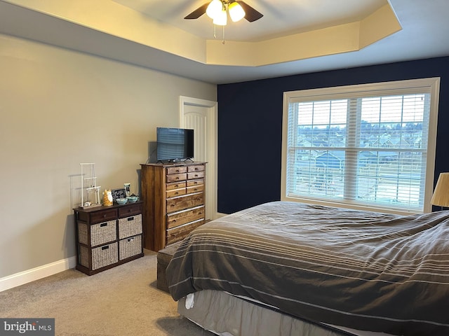 carpeted bedroom with baseboards, a tray ceiling, and ceiling fan