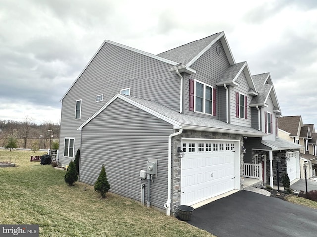 view of side of home with an attached garage, roof with shingles, aphalt driveway, and a yard